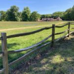 Photo of a wooden post and rail fence bordering an open grassland with a large house in the distance
