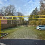 Photo of a yellow metal height barrier leading to a concrete paved car park in a countryside setting