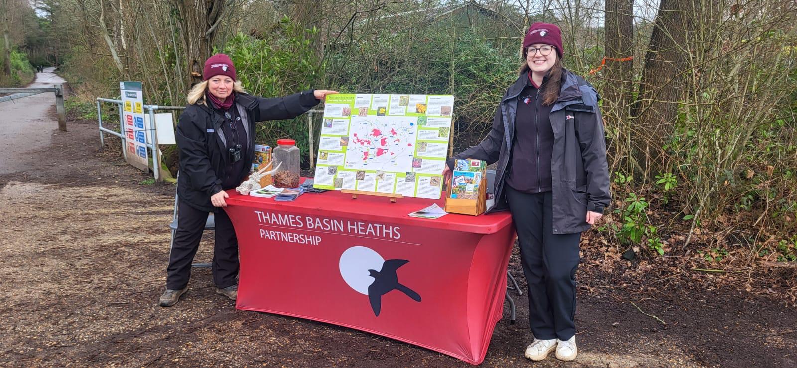 Photo of wardens Paula and Kay wearing Thames Basin Heaths Partnership uniform, standing at a table with project branding and display material