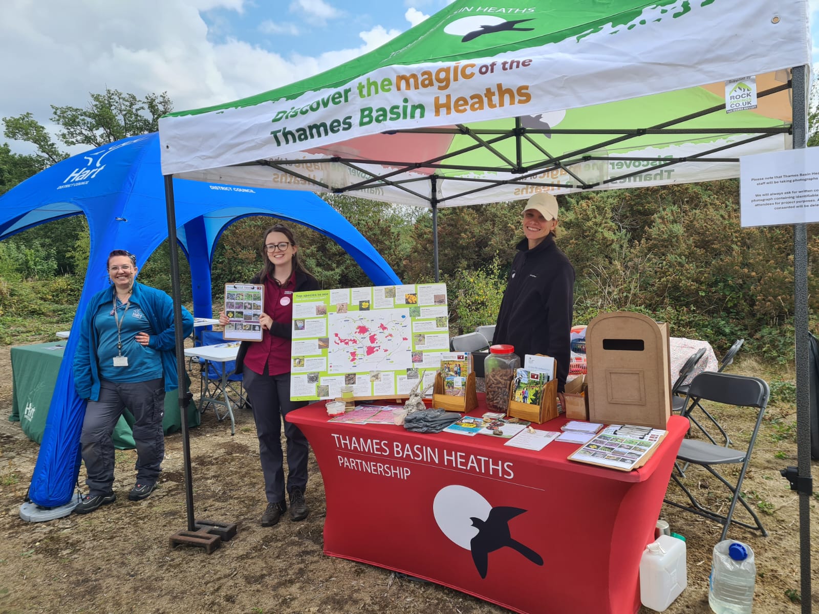 Photo of a Thames Basin Heaths Partnership branded gazebo alongside a Hart District Council gazebo with staff posing and smiling 