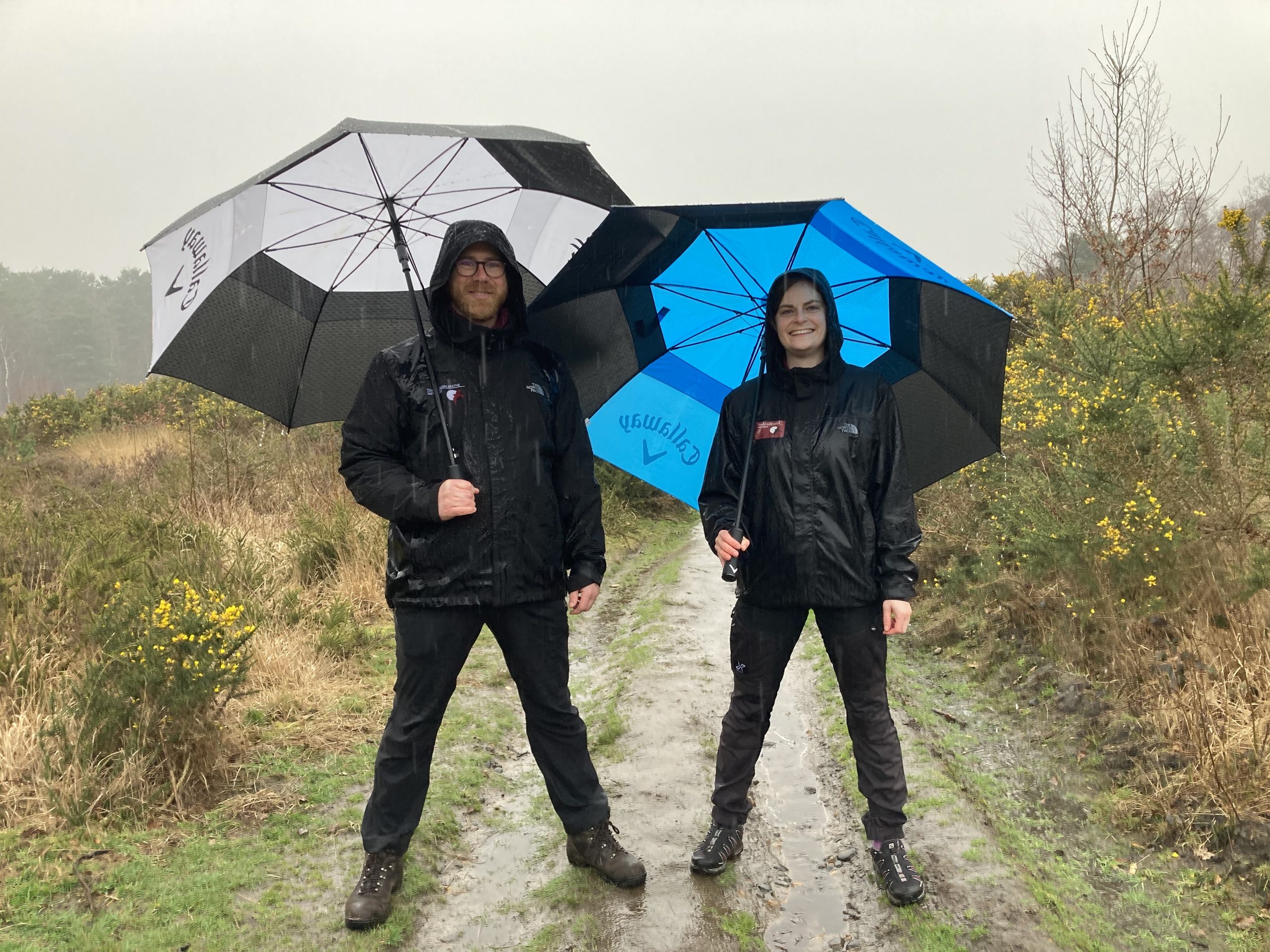 Photo of seasonal wardens Mick and Sophie carrying umbrellas on a heath in torrential spring rain