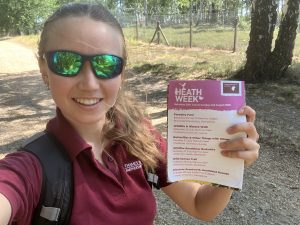 Photo of seasonal warden Sarah holding a Heath Week flyer